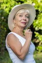 Street portrait of stylish and beautiful blonde woman 60-65 years old in a fashionable hat on the background of nature. Royalty Free Stock Photo