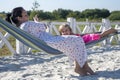 Street portrait of a woman about 40 years old, who is rocking a blonde little girl in a hammock. Mom and daughter relax on the bea