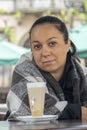 Street portrait of a 35-40-year-old woman sitting in a blanket at a table with a cup of latte coffee. Concept: open street restaur