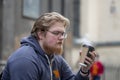 Street portrait of a young man with glasses and a beard 25-30 years old with blond hair drinking coffee from a paper cup against Royalty Free Stock Photo