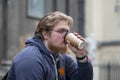 Street portrait of a young man with glasses and a beard 25-30 years old with blond hair drinking coffee from a paper cup against Royalty Free Stock Photo