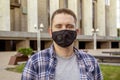 Street portrait of a young man 20-25 years old in a black medical mask on the background of modern city buildings. Royalty Free Stock Photo