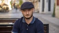 Street portrait of a young man 30 -35 years old in a cap with a beard, sitting on a bench and looking directly into the camera on Royalty Free Stock Photo