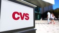 Street signage board with CVS Health logo. Blurred office center and walking people background. Editorial 3D rendering