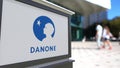 Street signage board with Danone logo. Blurred office center and walking people background. Editorial 3D rendering