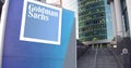 Street signage board with The Goldman Sachs Group, Inc. logo. Modern office center skyscraper and stairs background