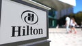 Street signage board with Hilton Hotels Resorts logo. Blurred office center and walking people background. Editorial 3D