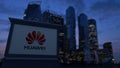 Street signage board with Huawei logo in the evening. Blurred business district skyscrapers background. Editorial 3D