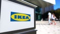 Street signage board with Ikea logo. Blurred office center and walking people background. Editorial 3D rendering