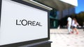 Street signage board with L`Oreal logo. Blurred office center and walking people background. Editorial 3D rendering