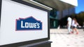 Street signage board with Lowe`s logo. Blurred office center and walking people background. Editorial 3D rendering