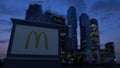 Street signage board with McDonald`s logo in the evening. Blurred business district skyscrapers background. Editorial 3D