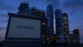 Street signage board with Siemens logo in the evening. Blurred business district skyscrapers background. Editorial 3D