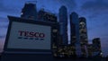 Street signage board with Tesco logo in the evening. Blurred business district skyscrapers background. Editorial 3D Royalty Free Stock Photo