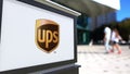 Street signage board with United Parcel Service UPS logo. Blurred office center and walking people background. Editorial Royalty Free Stock Photo