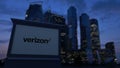 Street signage board with Verizon Communications logo in the evening. Blurred business district skyscrapers background