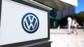 Street signage board with Volkswagen logo. Blurred office center and walking people background. Editorial 3D rendering