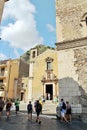 A street in a small Italian town with people walking, small town buildings and a church in the background