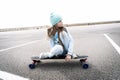 Street sports: A girl in a blue sweater and cap quickly rolls on a longboard.