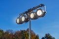 Street spotlight. Four round glowing lamps. Lighting of streets, objects, buildings. Blurred background of sky and trees