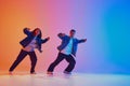 Street style. Two hip-hop dancers, man and woman, in motion against gradient studio background in neon lighting, filter. Royalty Free Stock Photo