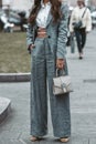 Street style, woman wearing white cropped shirt, a gray blazer jacket, gray matching suit pants, a beige leather handbag and