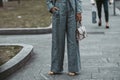 Street style, woman wearing white cropped shirt, a gray blazer jacket, gray matching suit pants, a beige leather handbag and