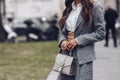 Street style, woman wearing white cropped shirt, a gray blazer jacket, gray matching suit pants, a beige leather handbag and