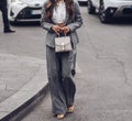 Street style, woman wearing white cropped shirt, a gray blazer jacket, gray matching suit pants, a beige leather handbag and