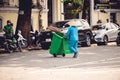 Street sweeper with a salakot hat carrying the garbage bin and a broom in Vietnam, Hanoi City