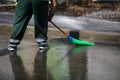 Street sweeper cleaning city sidewalk with water from a hose and a plastic broom - blue collar jobs