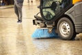 A street sweeper sweeps up a stone pavement with a strong brush in rainy weather. Maintaining clean tourist city. Preventing