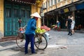 The street vendor with bike loaded of tropical fruits in old town street in Hanoi, old houses and street activites on background