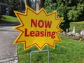 Street view of a bright yellow `Now Leasing` sign outside of a large apatment complex