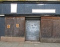 Street view of the front of an old abandoned shop with decaying boarded up windows covering the storefront and a closed steel Royalty Free Stock Photo