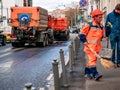 Street worker sweeping the sidewalk in an orange uniform. In the background, special watering machines are visible for cleaning s Royalty Free Stock Photo