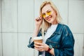 Streetstyle fashion look, pretty cool smiling young woman with coffee cup walking in city, happy female model wearing trendy