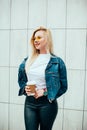 Streetstyle fashion look, pretty cool smiling young woman with coffee cup walking in city, happy female model wearing trendy Royalty Free Stock Photo