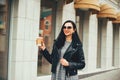 Streetstyle fashion look, pretty cool smiling young woman with coffee cup walking in city, happy female model wearing trendy Royalty Free Stock Photo