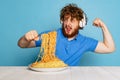 Emotive young hairy red-bearded man tasting large portion of noodles, pasta isolated on blue studio background.