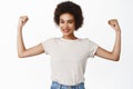 Strength and women workout concept. Smiling black girl with afro hair, young woman flexing biceps, showing muscles on