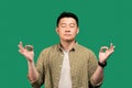 Stress relief concept. Asian man meditating with closed eyes, keeping calm searching for inner balance, green background Royalty Free Stock Photo