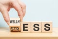 Stress or Wellness word concept on wooden cubes. Symbol of stress or well-being. Businessman hand turns the dice. blue background