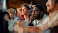 Stressed African Man Watching a Live Soccer Match on TV in a Sports Bar. Excited Fans Cheering and