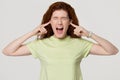 Stressed angry redhead woman sticking plug fingers in ears screaming