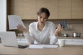 Stressed annoyed young laptop user woman reviewing domestic paper documents Royalty Free Stock Photo