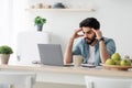 Stressed arab male entrepreneur having problems at work, sitting upset with laptop computer at kitchen table