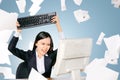 Stressed asian business woman with flying paper scattered want to slam the keyboard computer