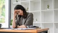 Stressed Asian businesswoman sits at her desk suffering from headache, having troubles Royalty Free Stock Photo