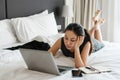Stressed Asian businesswoman working on laptop computer in bed at hotel. Business trip, people and technology concept, copy space Royalty Free Stock Photo